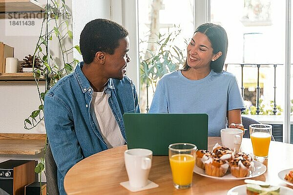 Multiethnisches Paar  das beim Frühstück einen Online Einkauf am Computer tätigt