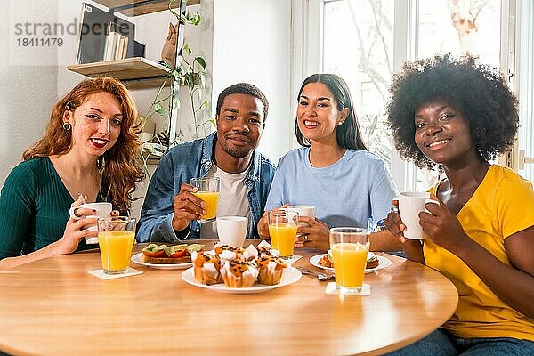 Multiethnische Freunde beim Frühstück mit Orangensaft und Muffins zu Hause