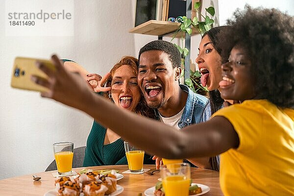 Multiethnische Freunde bei einem Frühstück mit Orangensaft und Muffins zu Hause  Selfie lächelnd und Spaß habend