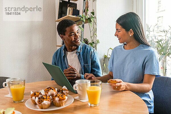 Multiethnisches Paar  das beim Frühstück mit dem Computer online einkauft  neben dem Fenster