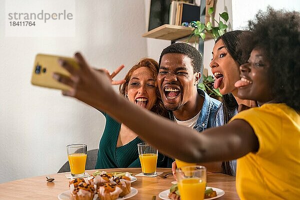 Multiethnische Freunde bei einem Frühstück mit Orangensaft und Muffins zu Hause  Selfie lächelnd