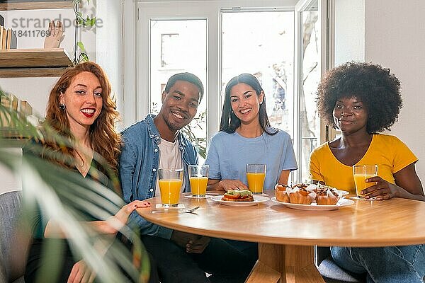 Porträt von multiethnischen Freunden beim Frühstück mit Orangensaft und Muffins zu Hause