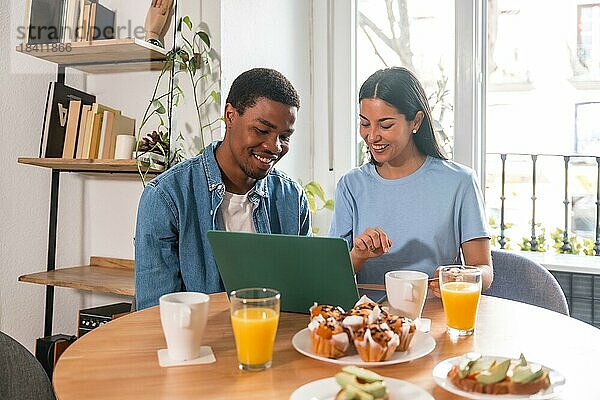 Multiethnisches Paar  das beim Frühstück einen Online Einkauf am Computer tätigt