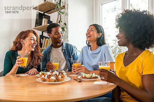 Multiethnische Freunde beim Frühstück mit Orangensaft und Muffins zu Hause