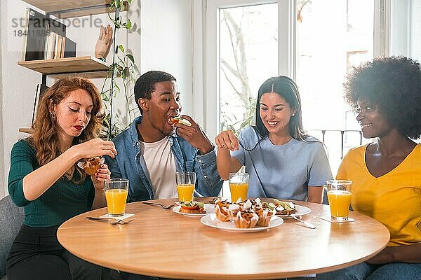 Multiethnische Freunde bei einem Frühstück mit Orangensaft und Muffins zu Hause  Details beim Schneiden der Toasts