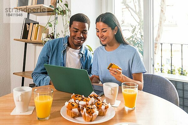 Pärchen beim Online Einkauf mit dem Computer  während sie frühstücken  neben dem Fenster  beim Einkaufen im Internet