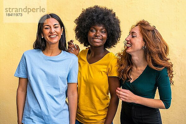 Porträt von schönen multiethnischen Freundinnen lächelnd auf einer gelben Wand