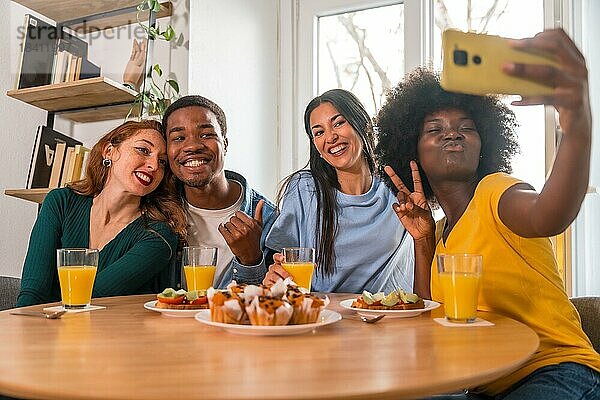 Multiethnische Freunde bei einem Frühstück mit Orangensaft und Muffins zu Hause  Selfie lächelnd