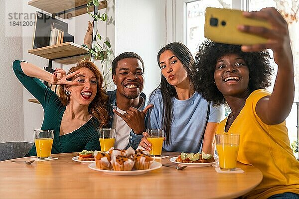 Multiethnische Freunde bei einem Frühstück mit Orangensaft und Muffins zu Hause  die ein Selfie machen