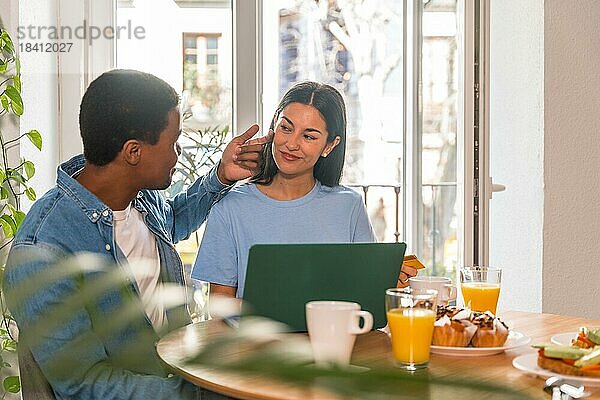 Pärchen  das beim Frühstück mit dem Computer online einkauft  neben dem Fenster  Mann streichelt sie