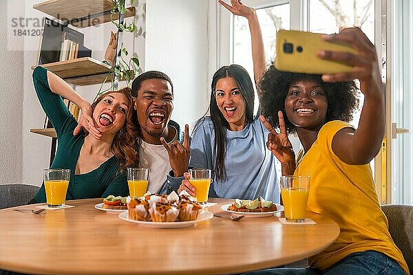 Multiethnische Freunde bei einem Frühstück mit Orangensaft und Muffins zu Hause  die ein Selfie machen