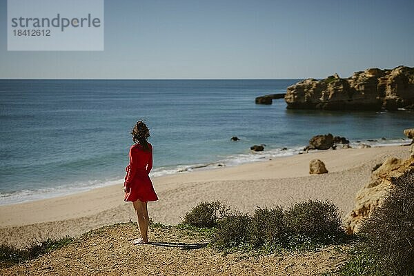 Attraktive Frau in rotem Kleid auf der Spitze der Klippen am Strand von Sao Rafael  Algarveküste Portugal