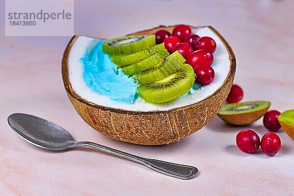 Frucht Smoothie Bowl in Kokosnussschale  natürlich gefärbt mit blauem Spirulina Pulver und garniert mit Cranberries und Kiwis