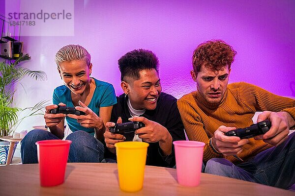 Gruppe junger Freunde  die zusammen auf dem Sofa zu Hause Videospiele spielen  lächelnd  junge Millennials