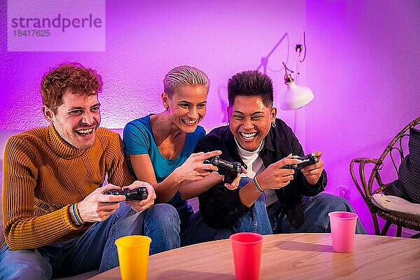 Gruppe junger Freunde  die zusammen auf dem Sofa zu Hause Videospiele spielen  lilafarben  die Spaß haben