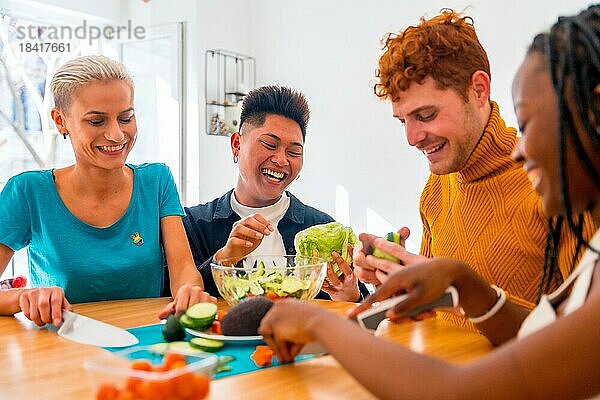 Porträt einer Gruppe von Freunden bei der Zubereitung vegetarischer Gerichte. Sie bereiten den Salat vor und haben Spaß im Haus