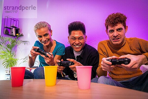 Gruppe junger Freunde  die zusammen auf dem Sofa zu Hause Videospiele spielen  lächelnd  junge Millennials