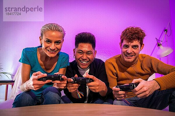 Gruppe junger Freunde  die zusammen auf dem Sofa zu Hause Videospiele spielen  lilafarben  konkurrierend in die Kamera blickend