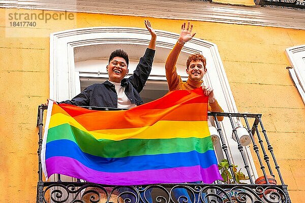 Homosexuell Junge Paare mit lgbt Flagge auf Balkon zu Hause Partei  winken lächelnd  LGBT Stolz