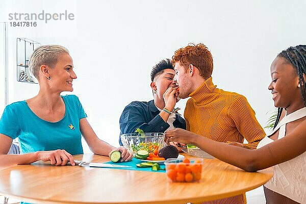 Gruppe von Freunden bereitet vegetarisches Essen zu. Vorbereitung der Salat und Spaß haben in der Küche  lgtb Junge Paar Kuss mit Karotte