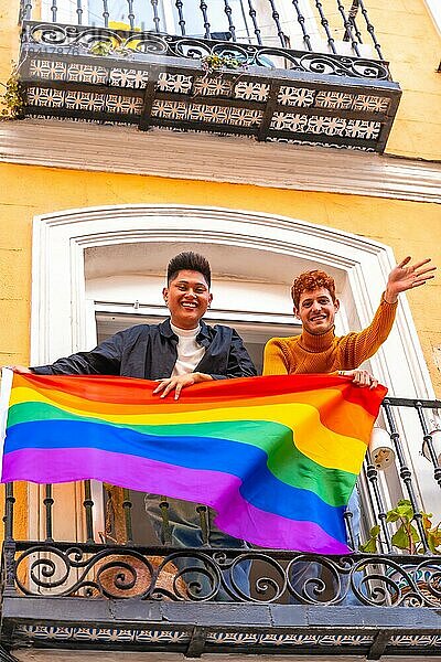 Homosexuell Junge Paare mit lgbt Flagge auf Balkon zu Hause Partei  winken lächelnd  LGBT Stolz