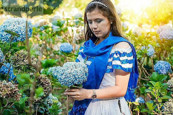 Frau in traditioneller mittelamerikanischer Volkstracht hält Blumen in einer Gärtnerei. Schöne Frau in nationaler Tracht hält Blumen in einer Gärtnerei. Nicaraguanische Volkstracht