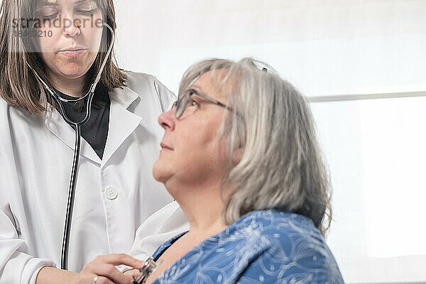 Junge Ärztin  die mit ihrem Stethoskop einen Patienten abhört  vor einem weißen Hintergrund