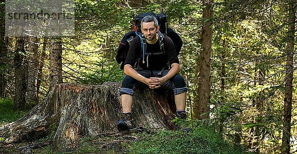 Ein Mann sitzt mit einem Rucksack auf einem Baumstamm am Wegesrand. Dolomiten  Italien  Dolomiten  Italien  Europa
