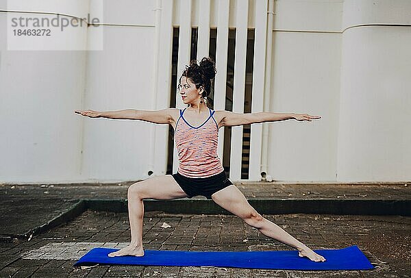 Mädchen übt Yoga Warrior II Pose im Freien. Lateinische Frau übt Yoga Krieger Pose im Freien. Junge Frau macht Yoga virabhadrasana II im Freien