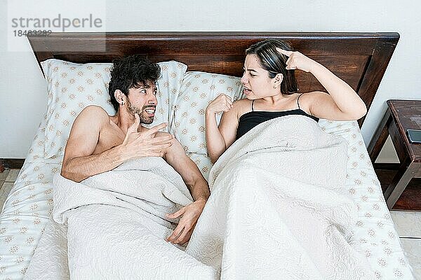 Aufgeregtes Paar  das im Bett liegt und sich streitet. Draufsicht auf ein junges Paar  das im Bett liegt und sich streitet. Eheprobleme Konzept