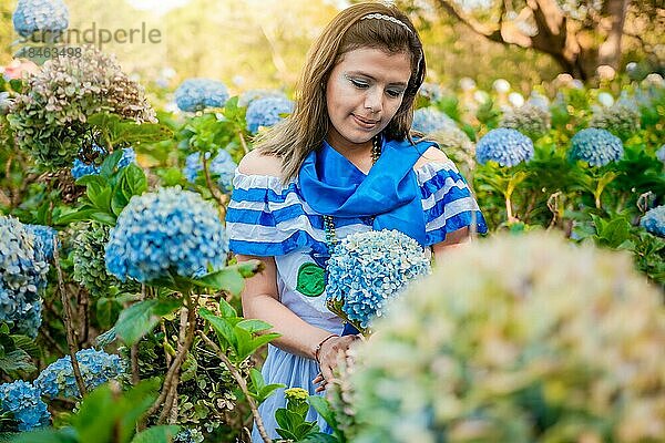 Porträt eines Mädchens in traditioneller mittelamerikanischer Volkstracht  das in einer Gärtnerei Blumen hält. Schöne nicaraguanische Frau in nationaler Volkstracht hält Blumen in einer Gärtnerei