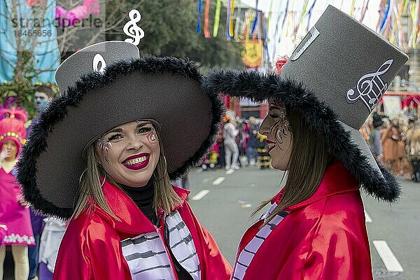 Zwei lächelnde Mädchen in roten Mänteln mit einer Tastatur und großen Zylindern auf dem Kopf beim Karneval in der Stadt Rijeka  Kroatien  Europa