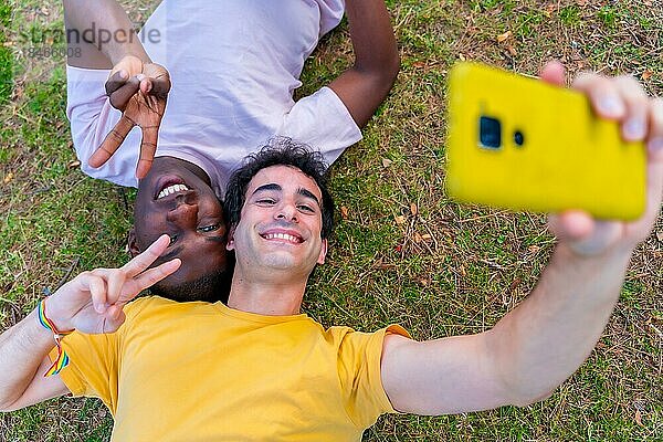 Paar multiethnische Männer in einem Park  lgbt Konzept  auf dem Gras liegend  ein Selfie machen