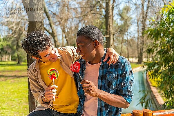 Paar multiethnische Männer  die einen Lutscher essen  lgbt Konzept  Spaß haben und lächelnd in einem Park