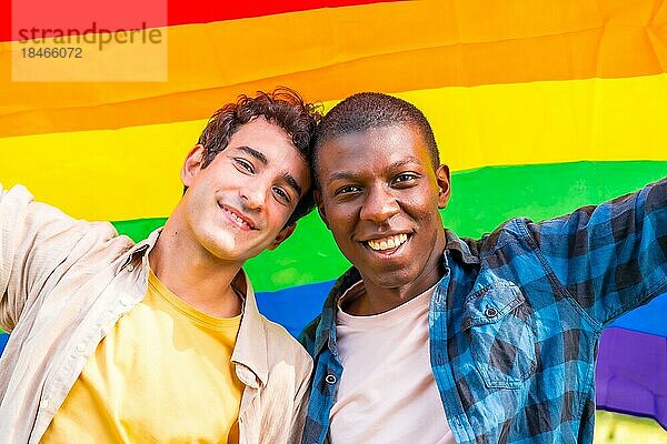 Porträt eines multiethnischen schwulen Paares  das eine Regenbogenflagge mit dem Symbol der Homosexualität hält