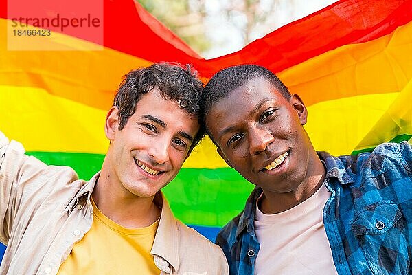 Porträt eines multiethnischen schwulen männlichen Paares  das eine Regenbogenflagge mit dem Symbol der Homosexualität hält  romantische Pose