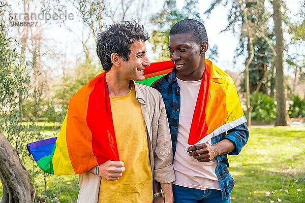 Multiethnisches schwules männliches Paar  das eine Regenbogenflagge mit dem Symbol der Homosexualität hält und Spaß hat