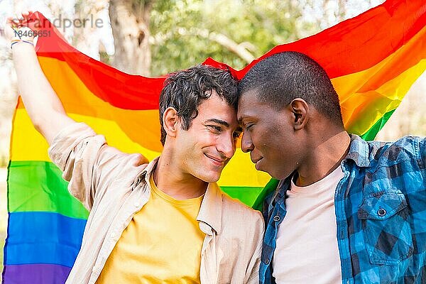 Multiethnisches schwules männliches Paar  das eine Regenbogenflagge mit dem Symbol der Homosexualität hält  romantische Pose