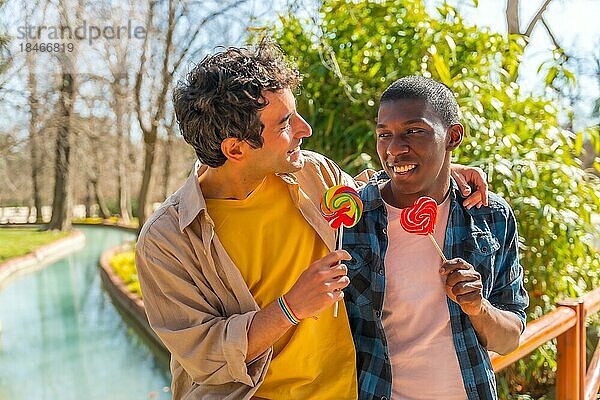 Multiethnisches schwules männliches Paar isst einen Lutscher  lgbt Konzept  hat Spaß und lächelt in einem Park