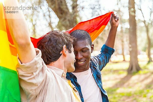 Multiethnisches schwules männliches Paar  das eine Regenbogenflagge mit dem Symbol der Homosexualität hält  romantische Pose