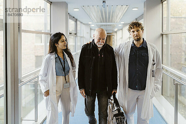 Lächelnde Ärztin  die an einem Kollegen mit einem Patienten in einem Krankenhausflur vorbeigeht