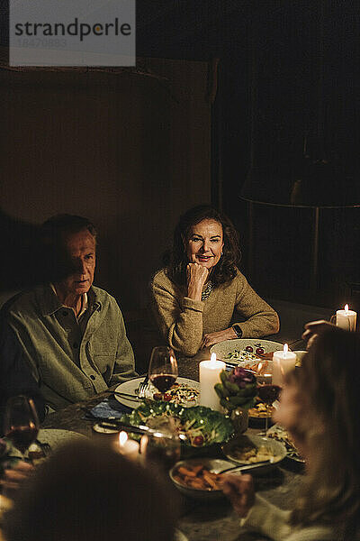 Älterer Mann und Frau sitzen bei Kerzenschein am Esstisch und feiern ein Abendessen