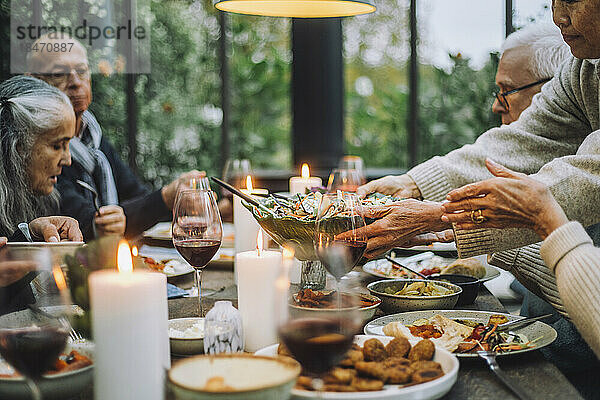 Ältere Frau serviert Salat für männliche und weibliche Freunde während einer Party