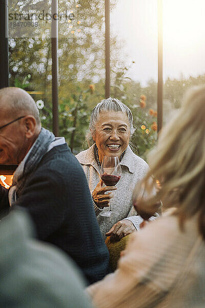 Glückliche ältere Frau hält ein Weinglas bei einer Dinnerparty