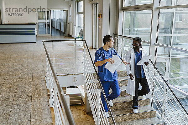 Männlicher Arzt und Krankenschwester diskutieren in voller Länge über Dokumente  während sie auf einer Treppe im Krankenhaus nach unten gehen