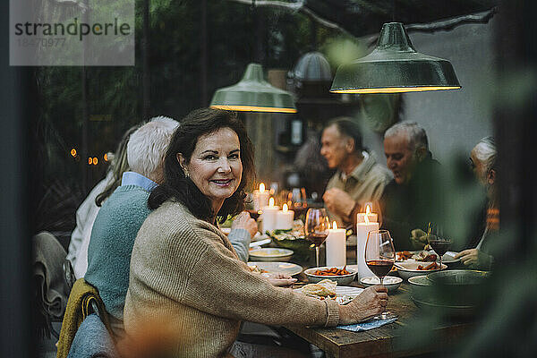 Porträt einer lächelnden älteren Frau  die sich mit Freunden bei einer Dinnerparty amüsiert