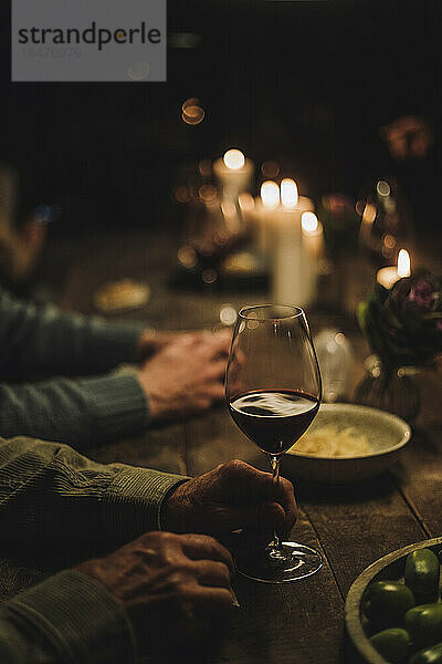 Die Hand eines älteren Mannes hält ein Weinglas am Esstisch während einer Party