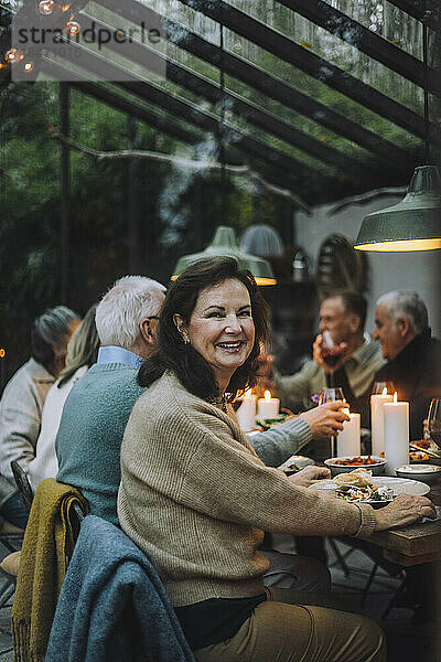 Porträt einer glücklichen Frau im Ruhestand  die während einer Dinnerparty mit Freunden auf einem Stuhl sitzt