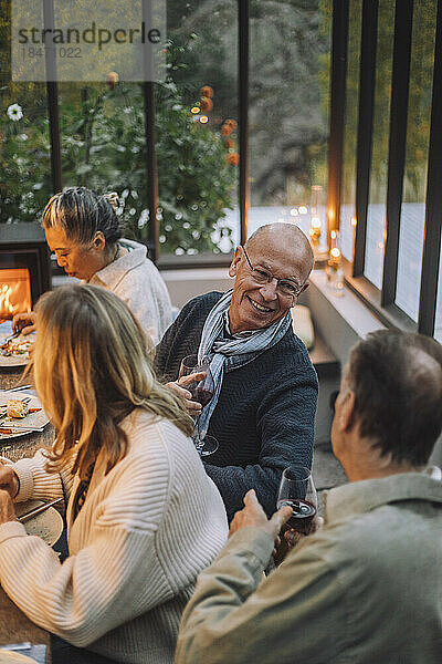 Lächelnder älterer Mann im Gespräch mit einem männlichen Freund im Ruhestand während einer Dinnerparty