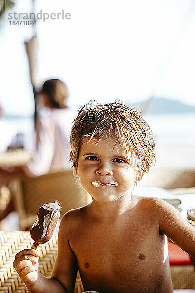Porträt eines lächelnden Jungen  der an einem sonnigen Tag in einem Ferienort ein Eis isst